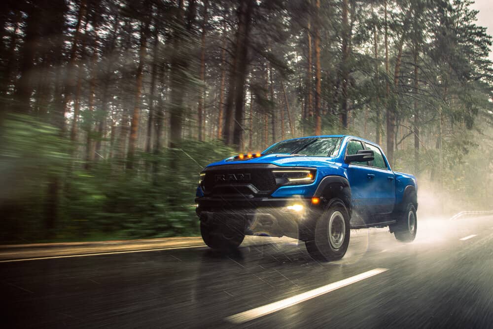 Blue lifted Ram truck driving down a dirt road in a forest. 