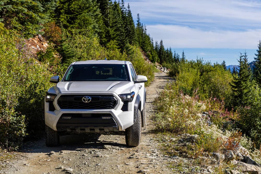 2024 Toyota Tacoma TRD pickup truck navigating scenic off-road trail in mountainous terrain.